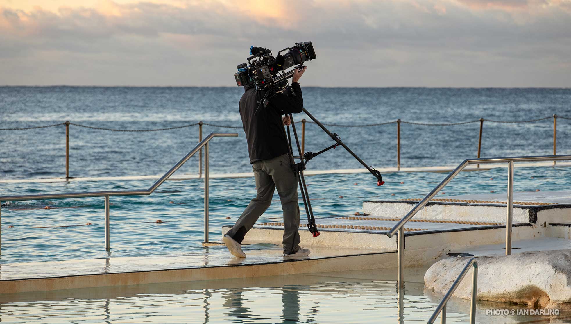 Camera operator lugging camera between pools
