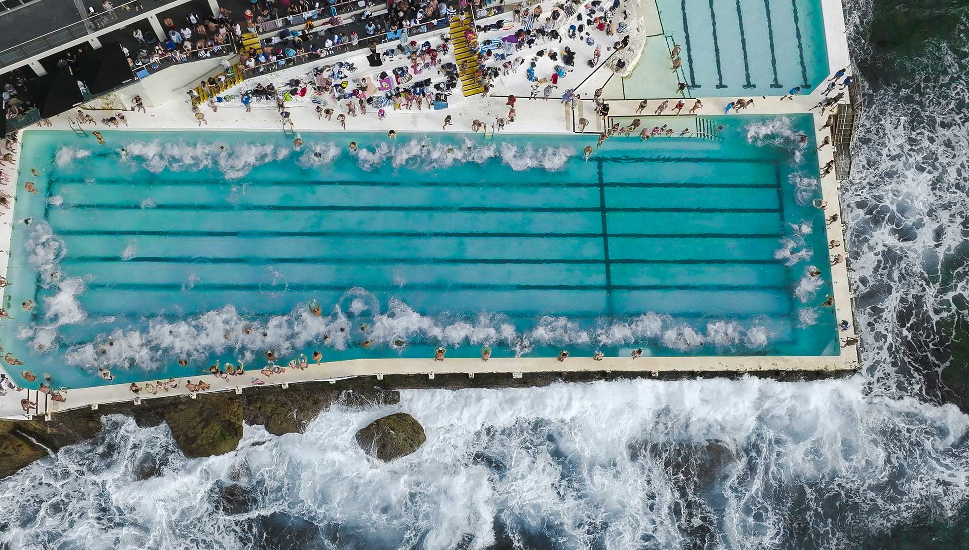 Drone shot from above showing swimmers all jumping into the Bondi Icebergs pool together